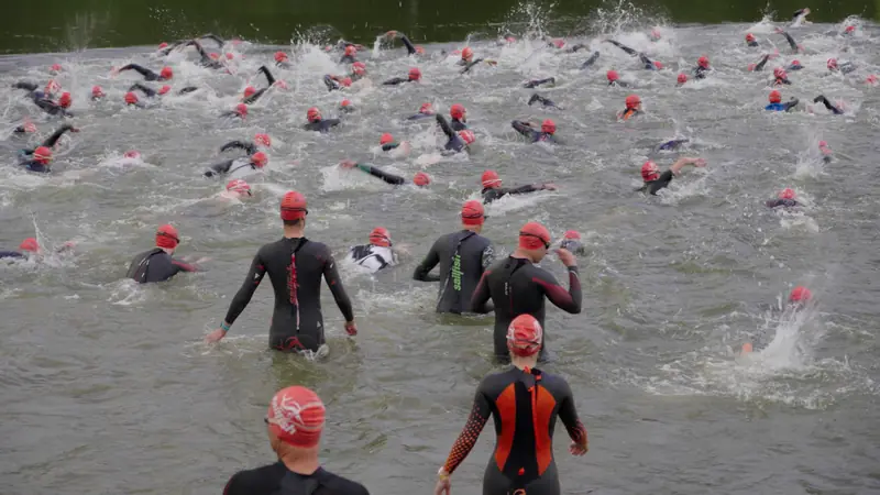 Schwimmstart: Athletinnen und Athleten mit roten Badekappen laufen ins Wasser
